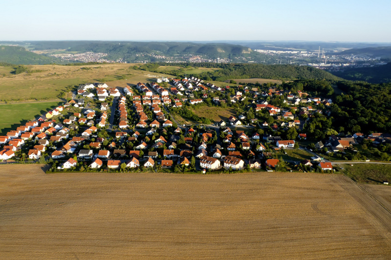 Der Ortsteil Cospeda mit Wohnhäusern, Feld, Wiese, Wald und dem Jenaer Tal im Hintergund.