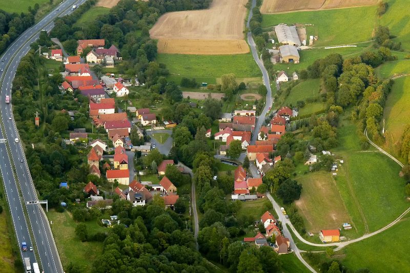Der Ortsteil Leutra mit Wohnhäusern, Feldern, Wiesen und der Autobahn 4 auf der linken Seite.