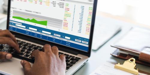 Laptop mit statistischen Grafiken auf einem Schreibtisch, ein Mann schreibt auf der Tastatur
